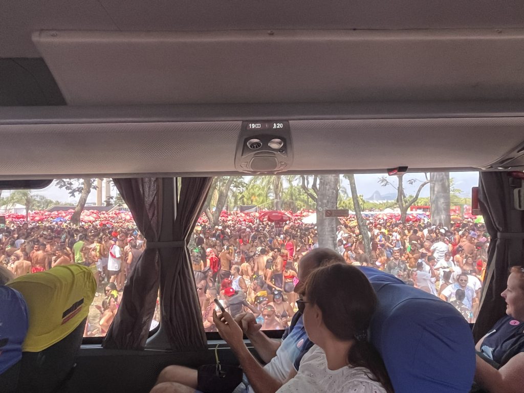 Dense Carnival crowd with red umbrellas seen through a tour bus window in Rio de Janeiro