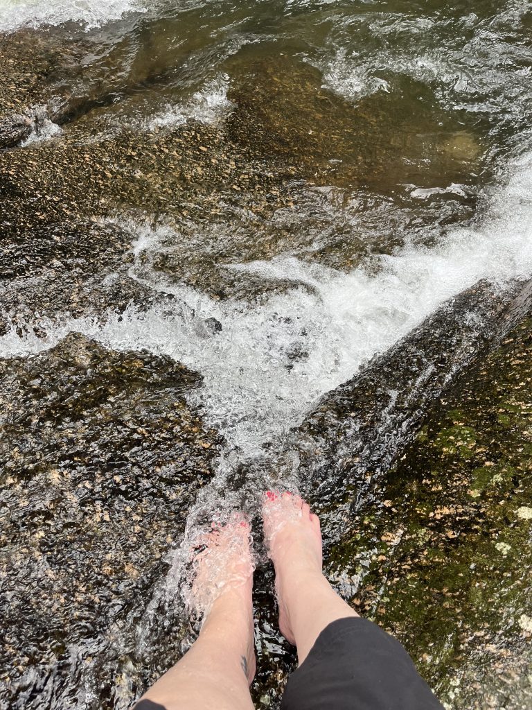 Feet standing in flowing water at the base of Pedra Branca waterfall