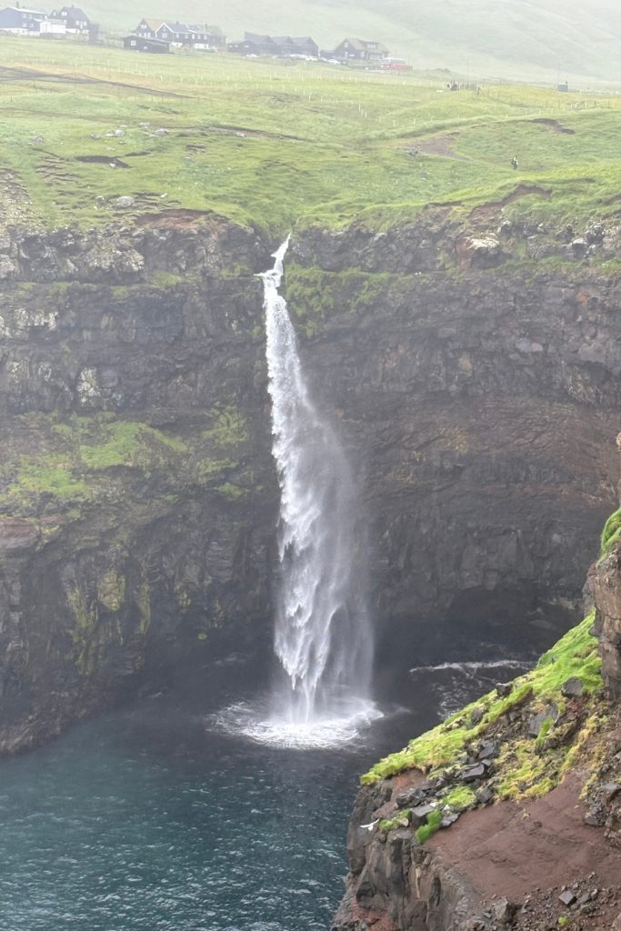 Múlafossur waterfall dropping into a cove near Gásadalur, with the village visible in the distance