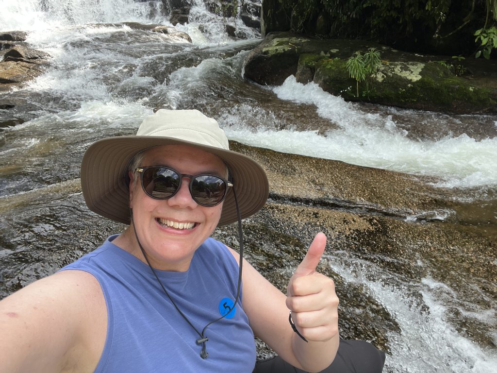 Woman giving a thumbs up in front of Pedra Branca waterfall in Paraty, Brazil