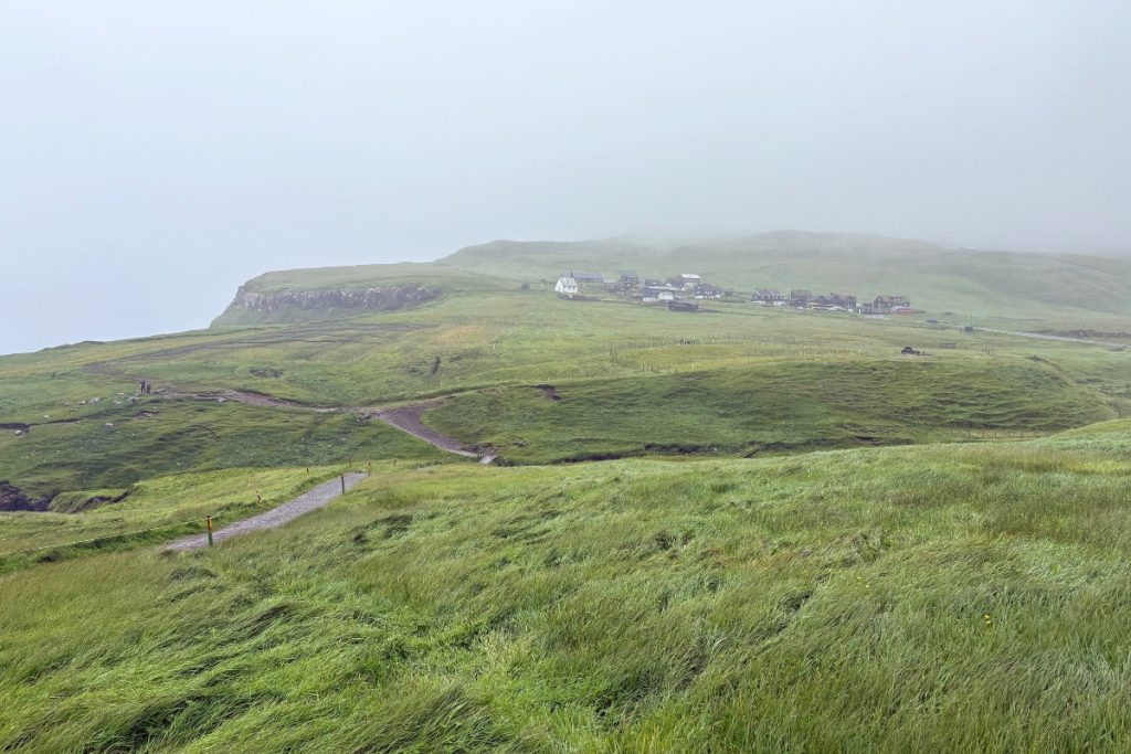 A grassy walking path with rope trail markers leading toward the village of Gásadalur, Faroe Islands