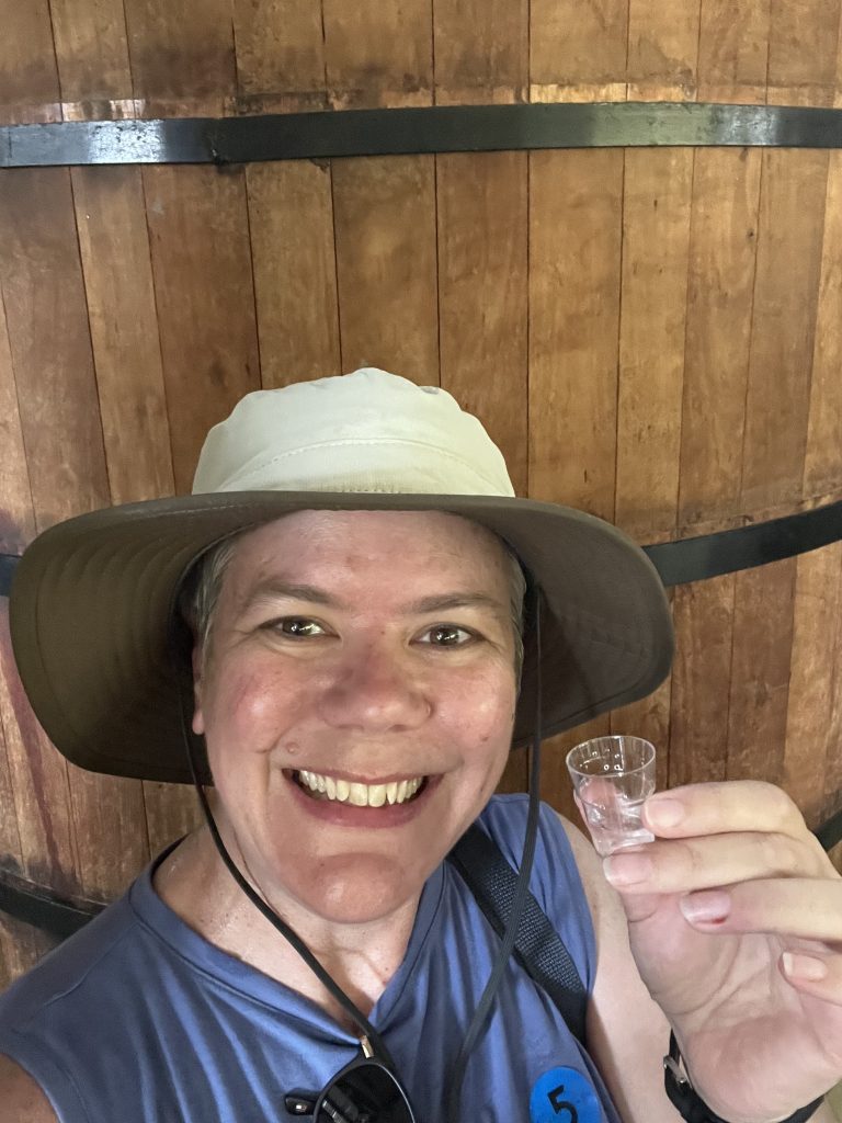 Woman holding a small tasting glass of cachaça inside a wooden barrel room at Pedra Branca distillery