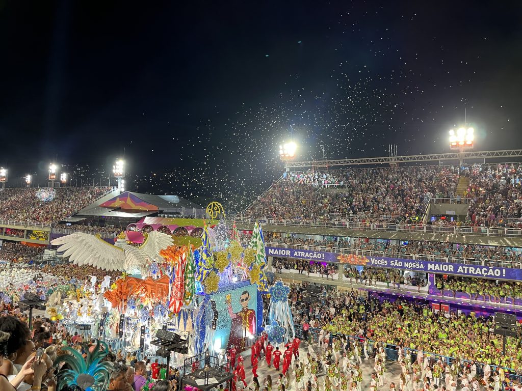 Confetti falling over the crowd at the Sambódromo during Rio Carnival, with a Maior Atração banner visible