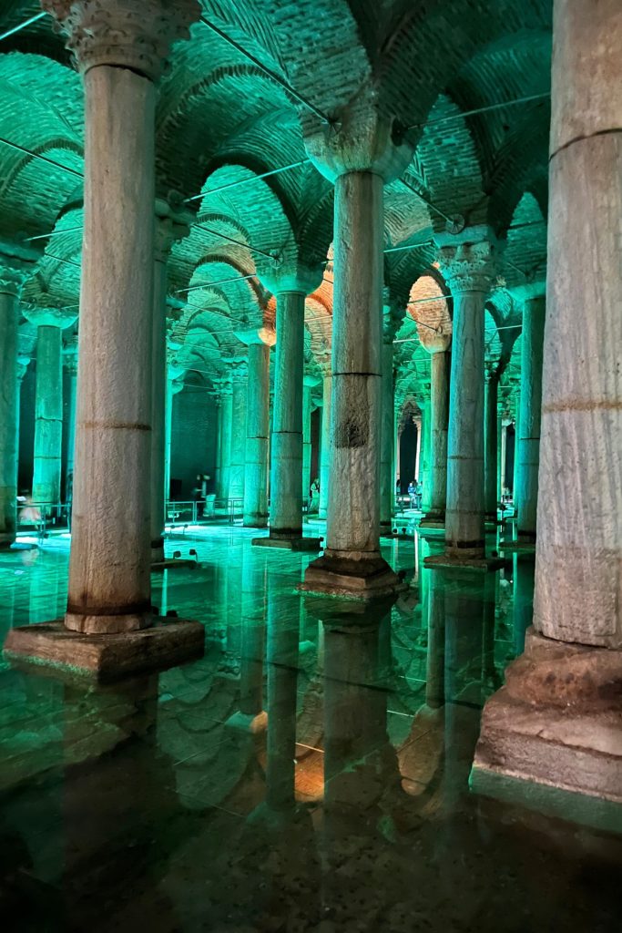 Rows of stone columns reflected in still water, lit in teal and blue, inside the Basilica Cistern.