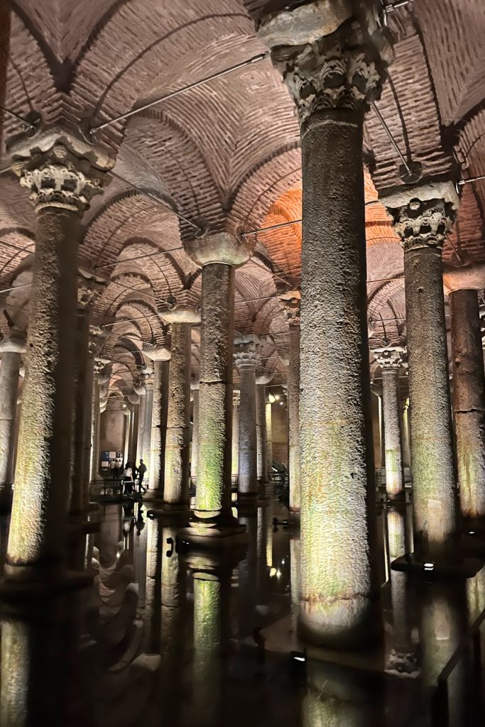 Close-up view of textured stone columns with carved capitals supporting brick vaulted arches inside the Basilica Cistern.