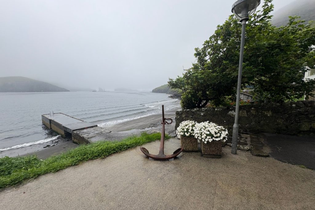 A coastal path with an anchor and flowers overlooking the fjord near Bøur, Faroe Islands