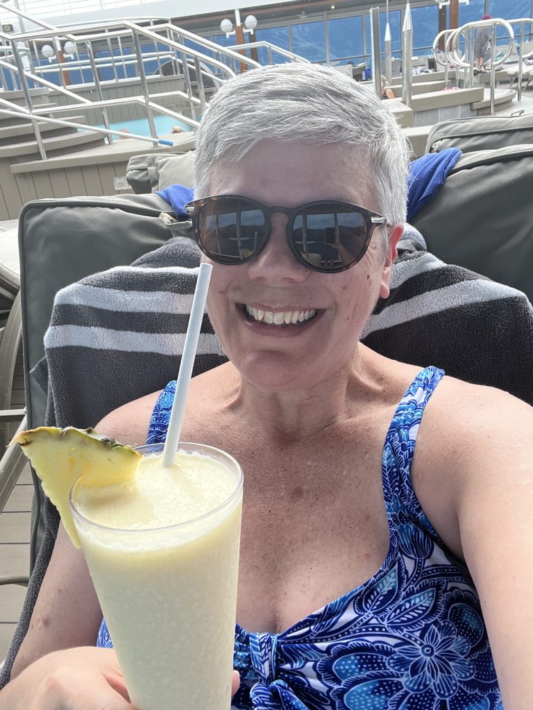 Woman holding a piña colada by the pool on a cruise ship after visiting Paraty, Brazil