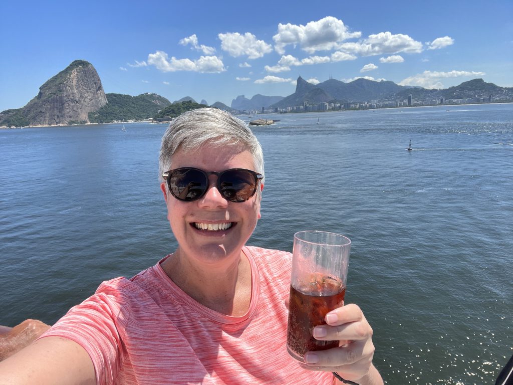 Selfie with a drink on a cruise ship deck, Sugarloaf Mountain and Christ the Redeemer statue visible in the background in Rio de Janeiro