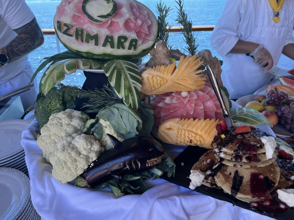 Watermelon carved with the Azamara logo, surrounded by fruit and vegetable garnishes on a cruise ship