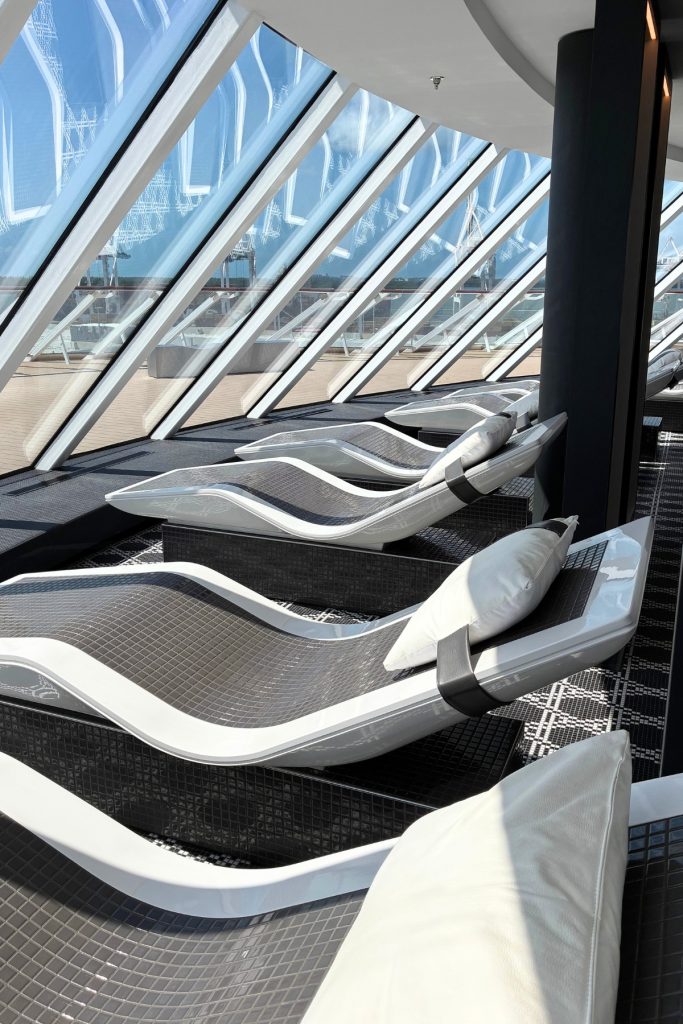 Spa relaxation loungers on Celebrity Beyond beneath glass-paneled windows overlooking the water