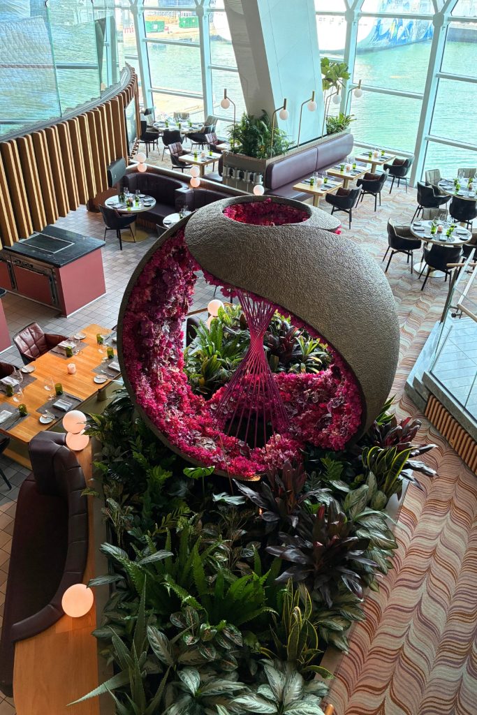 Eden restaurant on Celebrity Beyond with floral sculpture, greenery, and floor-to-ceiling windows