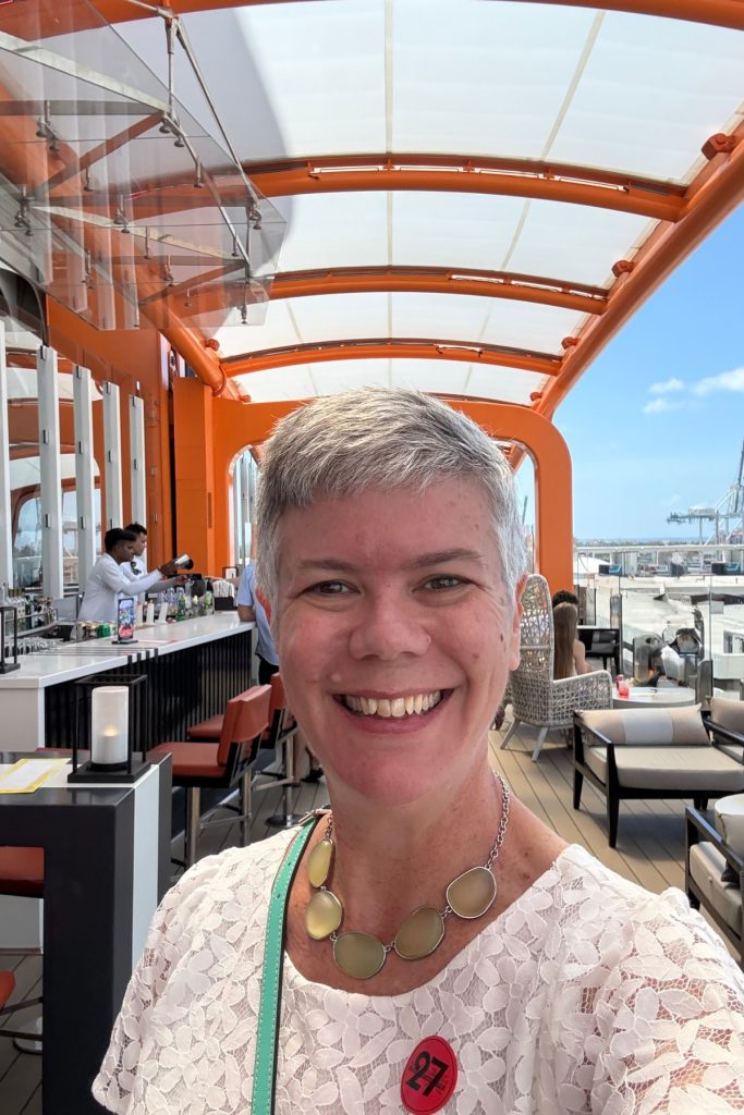 A woman smiling on Celebrity Beyond's Magic Carpet with bar and skyline in the background