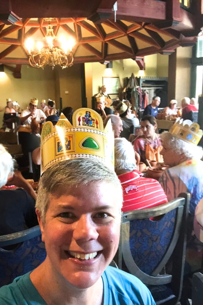 Selfie at a Hungarian restaurant lunch stop wearing a paper crown, with other cruise passengers seated at long tables in the background.