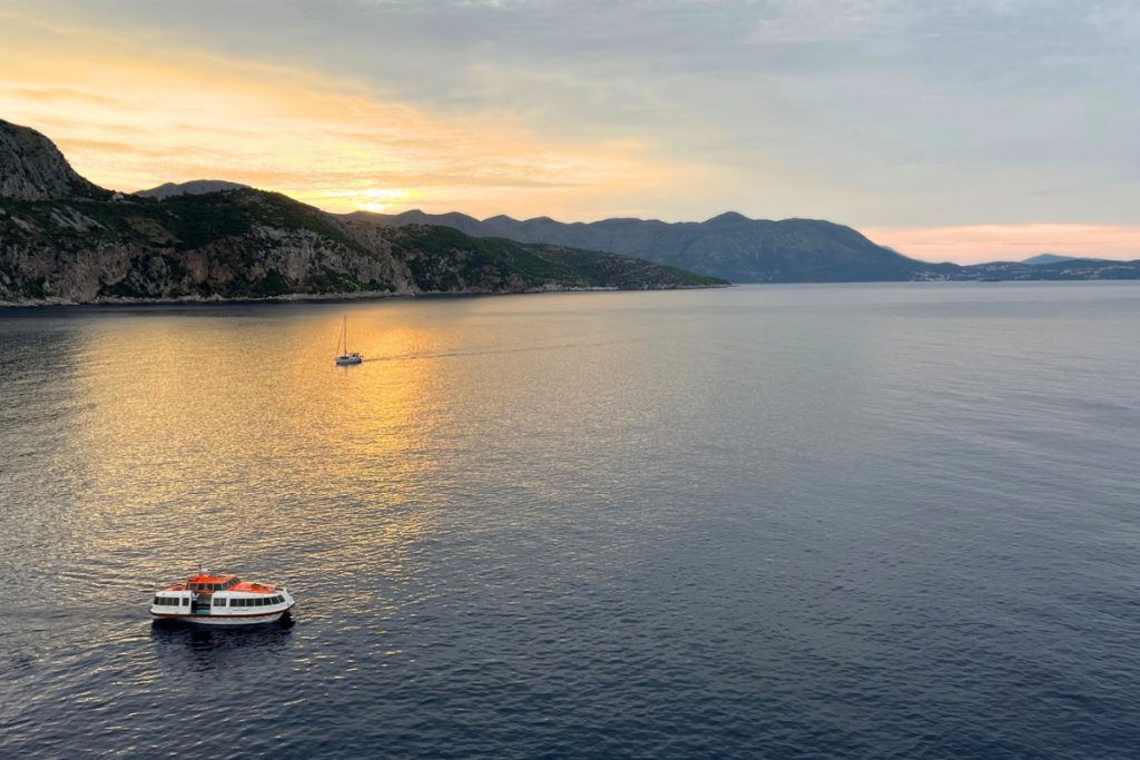 Small boats on calm water at sunrise near the Dubrovnik coastline, with mountains in the background