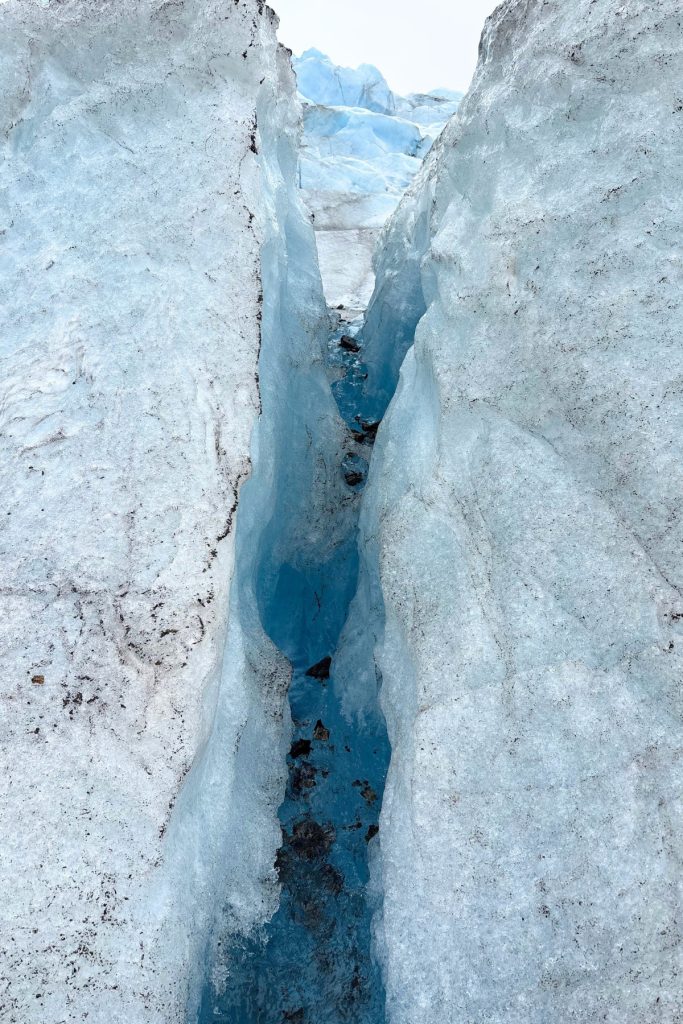 A narrow crevasse cutting deep into Mendenhall Glacier, its walls fading from white ice into deep blue at the bottom.