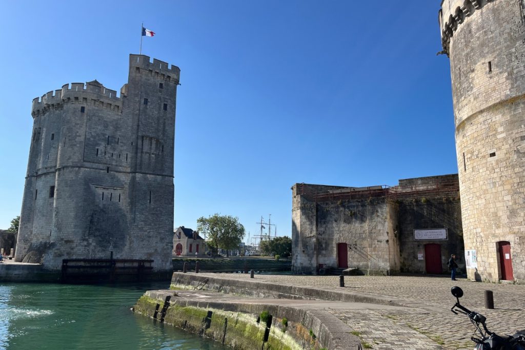 Tour Saint-Nicolas and Tour de la Chaîne medieval stone towers flanking the harbor entrance in La Rochelle, France, with a French flag flying atop the left tower.