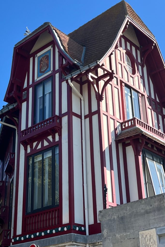 La Maison du Chat, a red and white timber-framed house in Norman Revival style in La Rochelle, France, with a small ceramic cat figure visible on the roof peak.