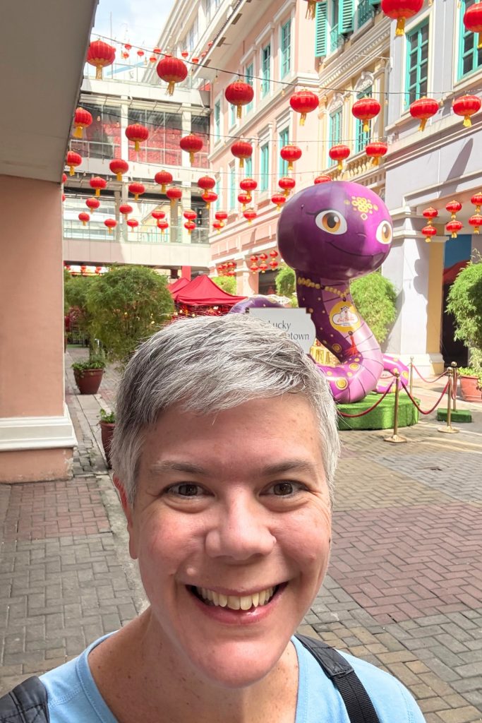 Woman smiling for a selfie in front of a giant inflatable purple snake mascot at Lucky Chinatown Mall in Manila