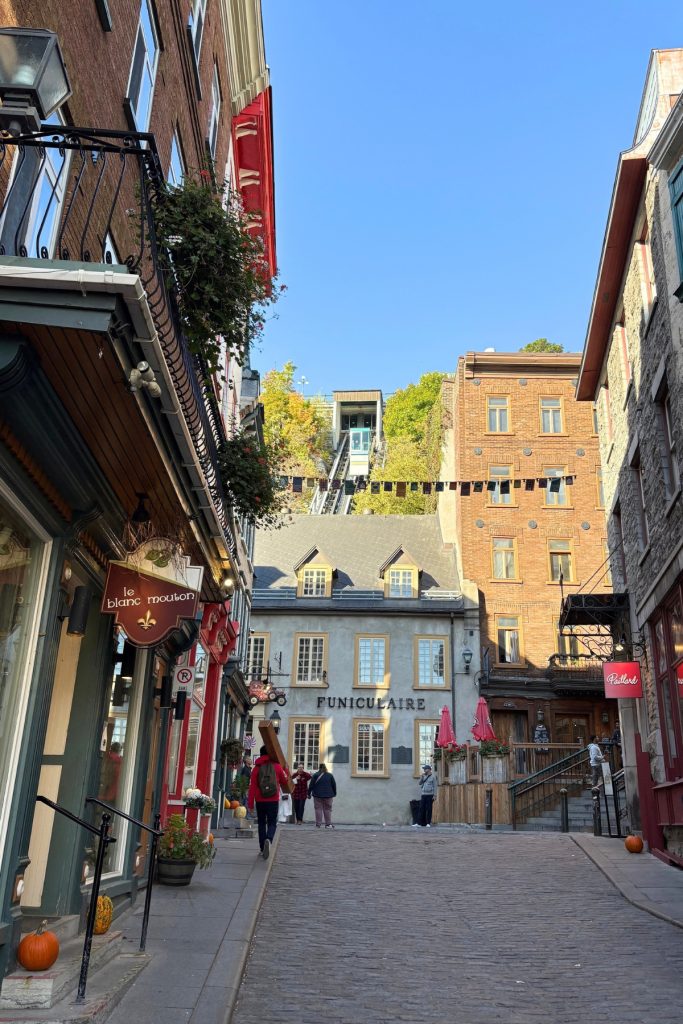 Funicular car descending a hillside track above a Quebec City street lined with shops, with the FUNICULAIRE sign visible on the station building.