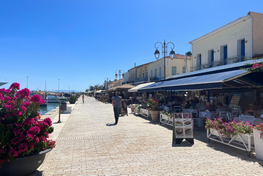 Waterfront promenade with flowering plants, cafés, and pedestrians in Katakolon, Greece