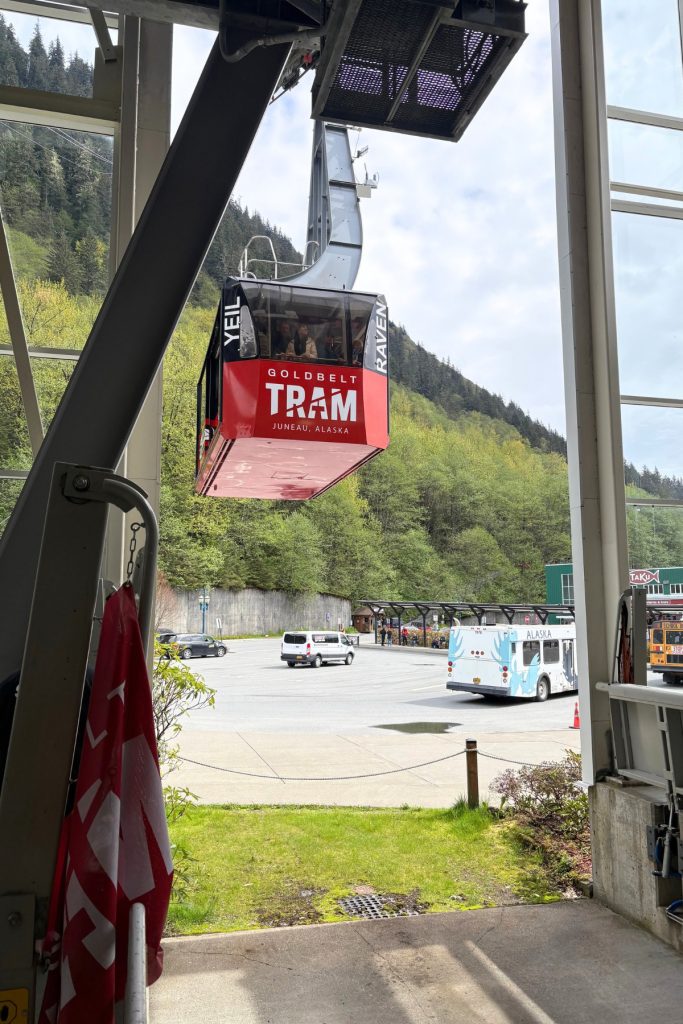 A red and black Goldbelt Tram gondola car suspended on a cable, arriving at its base station in downtown Juneau.
