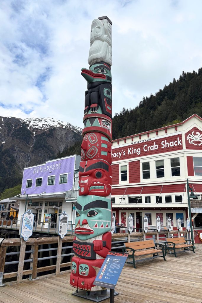A tall carved totem pole standing on Juneau's cruise pier boardwalk near Tracy's King Crab Shack.