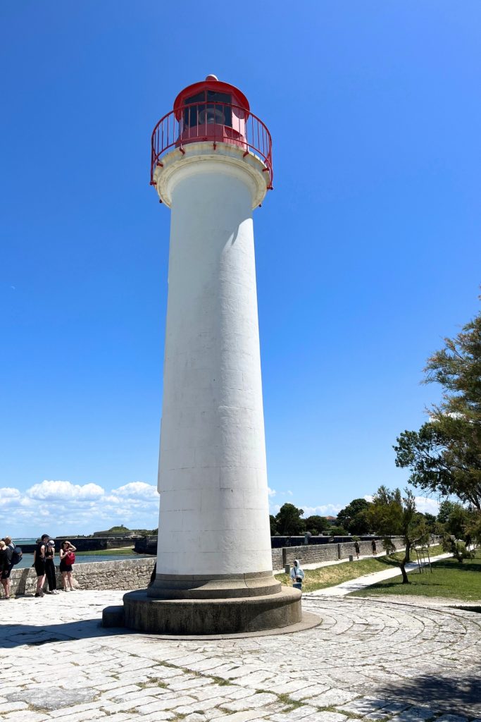 White lighthouse with a red lantern room, the Phare de Saint-Martin-de-Ré, standing against a clear blue sky on Île de Ré, France.