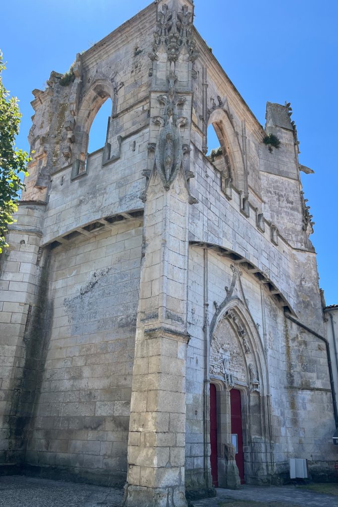 Weathered Gothic stone facade of Église Saint-Martin in Saint-Martin-de-Ré, Île de Ré, France, with battlements and open ruined arches above the entrance.