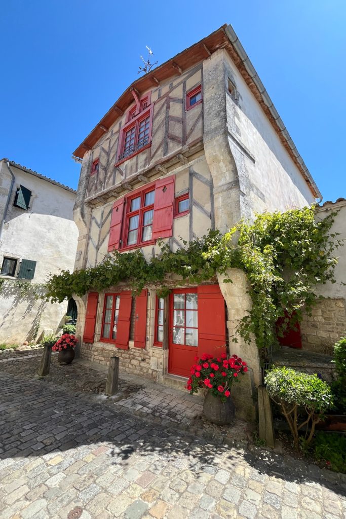 Half-timbered house with red shutters and window boxes of flowers on a cobblestone street in Saint-Martin-de-Ré, Île de Ré, France.