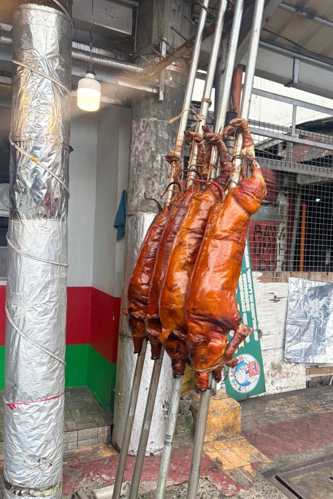 Four whole roasted lechon pigs hanging by their feet at a vendor stall in La Loma, Manila