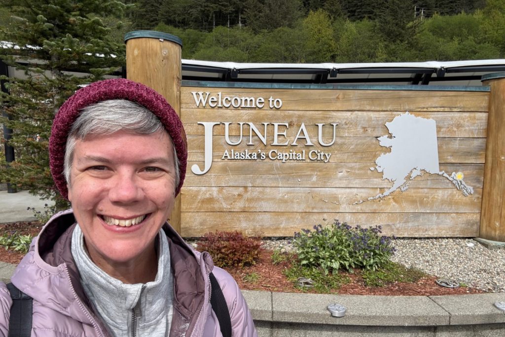 A woman smiling in front of the Welcome to Juneau sign in 2025.