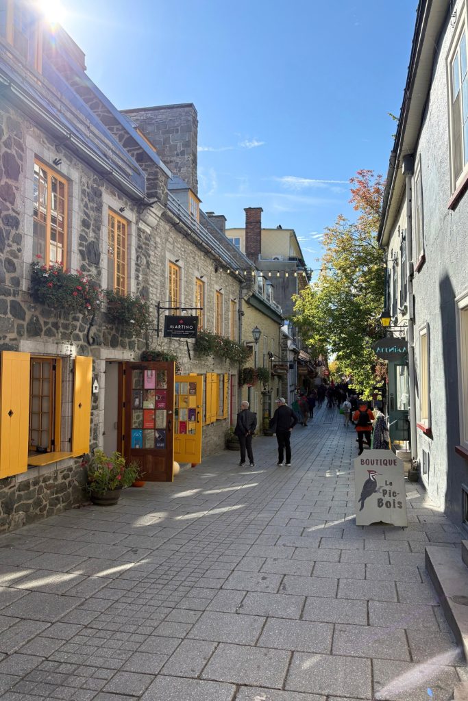 A cobblestone street in Quebec City's Petit-Champlain district, lined with stone buildings and yellow-shuttered shops.