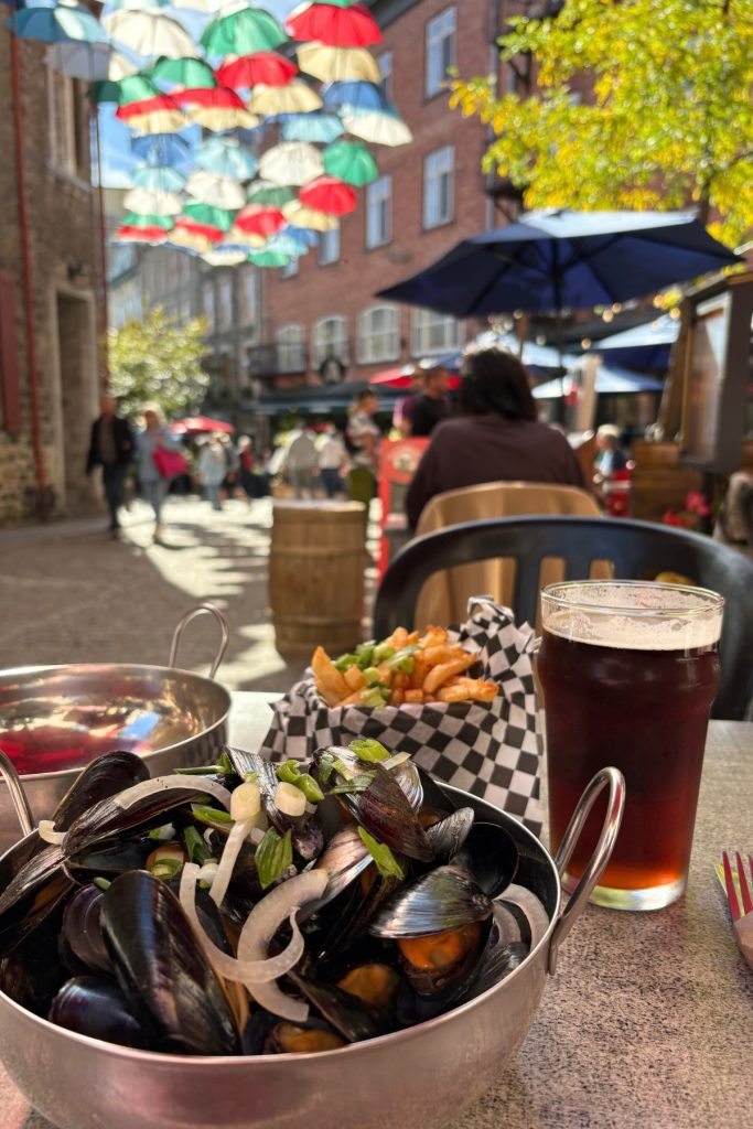 Mussels, fries, and a dark beer on a patio table under hanging umbrellas on Rue du Cul-de-Sac in Quebec City.