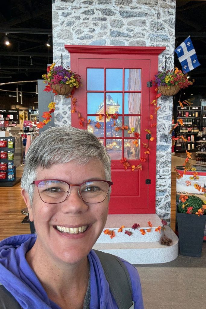 Selfie in front of a decorative red door display at the Quebec City airport, with a Château Frontenac photo in the window and a Quebec flag beside it.