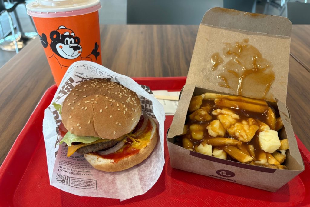 A burger, poutine, and a root beer with the A&W bear on the cup, on a red tray at the Quebec City airport.