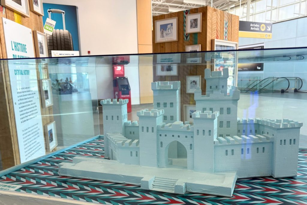 A white model castle representing Bonhomme Carnaval's ice palace, displayed in a glass case at the Quebec City airport.