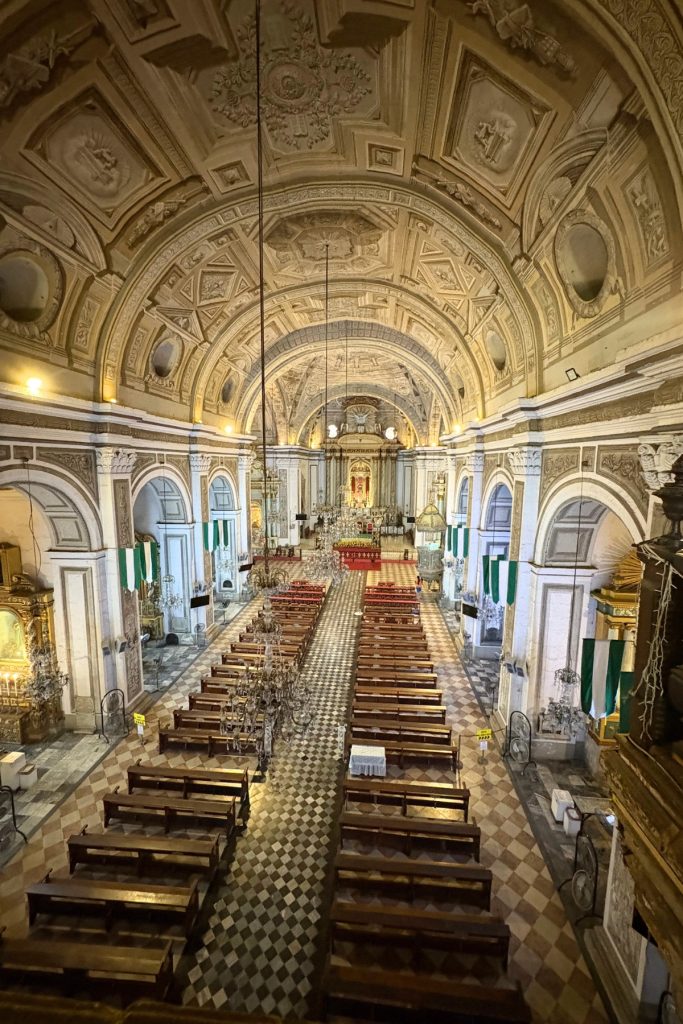 Nave of San Agustin Church with trompe l'oeil ceiling murals, chandeliers, and green and white ceremonial banners