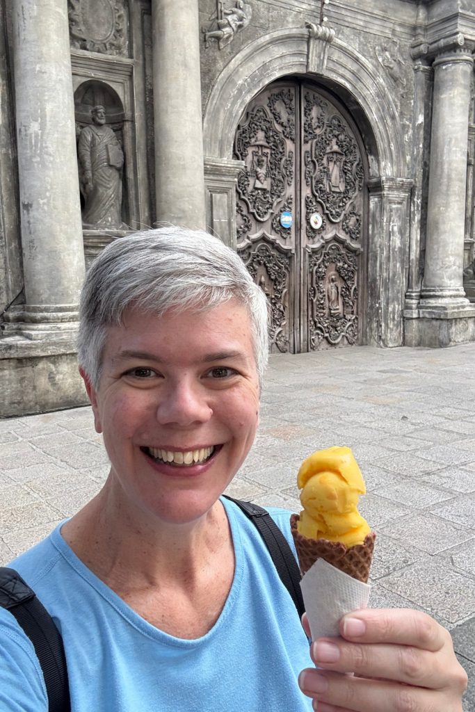 Woman holding a mango sorbetes cone in front of the carved wooden doors of San Agustin Church in Intramuros, Manila