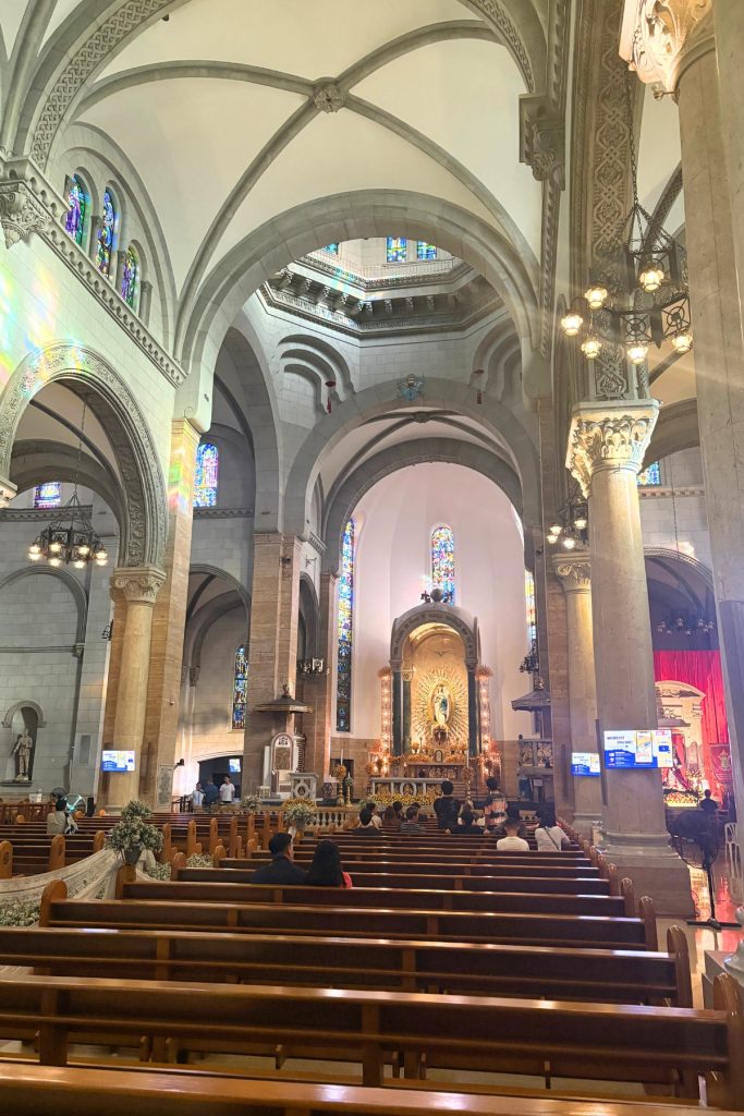Interior of Manila Cathedral with vaulted stone arches, stained glass, and a golden shrine to Our Lady at the altar