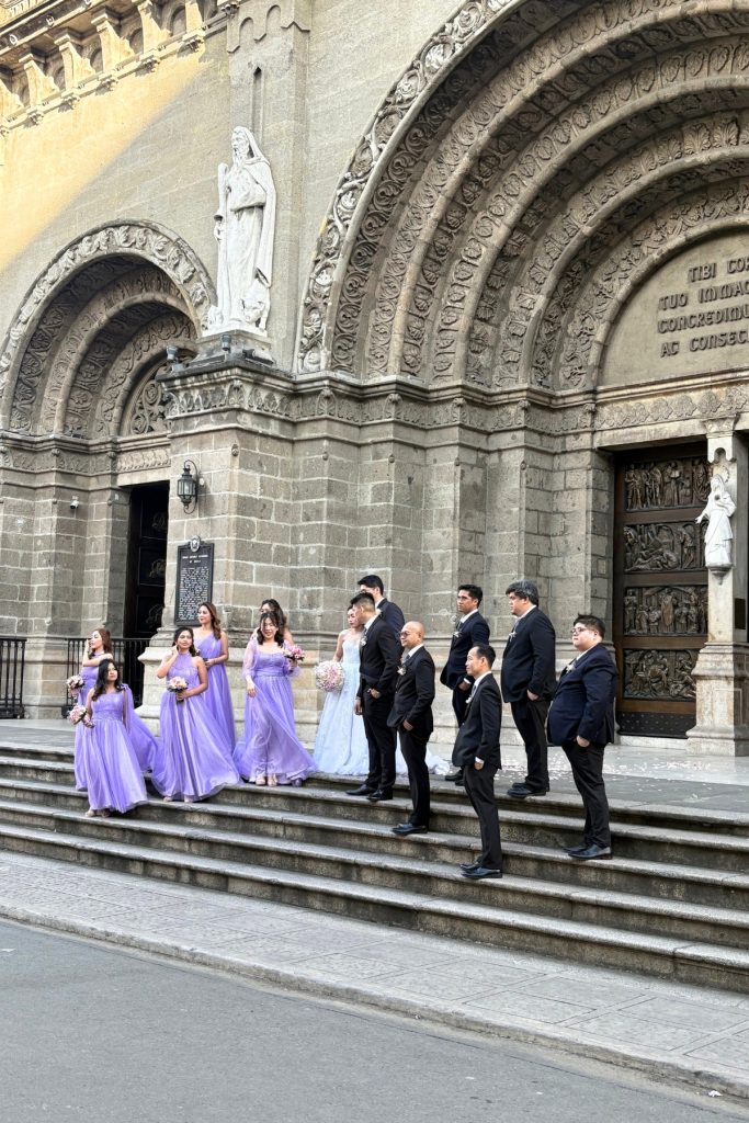 Wedding party in lavender dresses and black suits posing on the front steps of Manila Cathedral in Intramuros