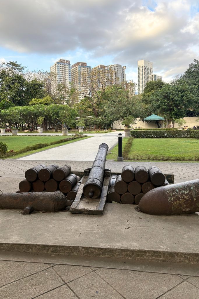 Old cannons on display at Fort Santiago in Manila, pointed toward a backdrop of modern high-rise buildings