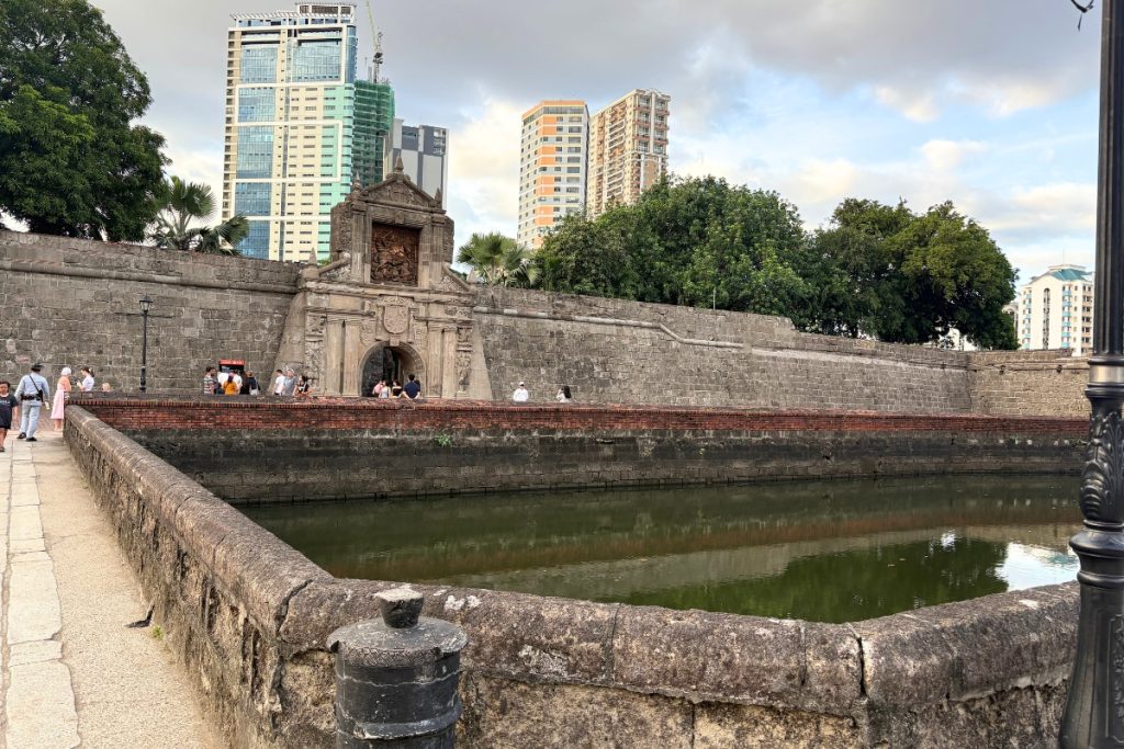 Moat and stone gate of Fort Santiago in Intramuros, Manila, with modern high-rise buildings in the background