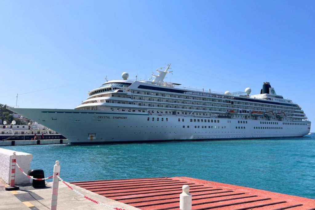 Crystal Symphony cruise ship docked at a red and gray pier in Kusadasi, Turkey, on calm teal water under a clear blue sky, illustrating cruise travel insurance.